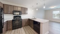 Located at 1745 Brooklyn Dr in Murray, Kentucky, this single-floor, one-bedroom, one-bathroom residence offers a thoughtfully designed layout that maximizes its compact footprint. The open-concept kitchen serves as the centerpiece of the living area, featuring rich dark brown cabinetry, light-toned countertops, and a peninsula with a double-basin sink. A full suite of black appliances — including a range, dishwasher, microwave, and refrigerator — provides complete functionality. Three pendant lights hang above the peninsula, adding a modern, decorative touch. Wood-look luxury vinyl plank flooring runs throughout the main living and kitchen areas, contributing to a clean and cohesive aesthetic. The bedroom offers a generous footprint with soft carpeting underfoot and a large window fitted with horizontal blinds, allowing ample natural light to fill the room. A dedicated closet provides practical storage. The bathroom is finished with wood-look vinyl flooring, crisp white walls, and a full tub-shower combination with a towel bar. Clean white panel doors are used consistently throughout the unit, reinforcing the modern, move-in-ready character of the space. The overall design is bright, neutral, and contemporary, making it a versatile and functional home.