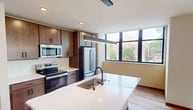 This contemporary 630 square foot apartment in Madison, WI offers a thoughtfully designed living space. The heart of the home is an open-concept kitchen featuring modern wood cabinetry, stainless steel appliances, and a spacious island with a sink, perfect for both meal preparation and casual dining. Large windows flood the living areas with natural light, offering views of the surrounding cityscape.

The bedroom, measuring 160 square feet, provides ample space and includes a ceiling fan for comfort. It features the same light-toned wood flooring found throughout the apartment, creating a cohesive aesthetic. The bathroom boasts a clean, modern design with a single vanity and a large mirror.

Throughout the apartment, recessed lighting and smooth, white ceilings contribute to the bright, airy feel. The neutral color palette and minimalist design allow for versatile decorating options. Despite its compact size, the layout efficiently utilizes every square foot, making this one-bedroom, one-bathroom apartment feel spacious and inviting. Located at 531 W Washington Ave, it offers urban living in a stylish, low-maintenance setting.