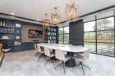 Located along I-85 N in Atlanta, GA, this single-floor amenity space combines contemporary design with functional versatility. The interior is anchored by a rich navy blue color palette, complemented by light tile flooring in a grid pattern and recessed lighting with tray ceiling details that add architectural depth.

The lounge area serves as the centerpiece, featuring a plush neutral sofa, cognac leather accent chairs, and layered patterned rugs. A textured brick-style accent wall frames a round mirror flanked by adjustable sconces, while floor-to-ceiling built-in shelving in navy displays curated décor. A large conference table with seating for several is positioned near expansive floor-to-ceiling windows, bathing the space in natural light and offering views of surrounding greenery. Pendant chandeliers with brass detailing hang above, lending an upscale ambiance.

The kitchenette is fully appointed with matte navy cabinetry extending to the ceiling, a white subway tile backsplash, stainless steel appliances including a dishwasher and oven, and a full-sized refrigerator. A large window brings in additional daylight. The entry corridor features secure package lockers and a wood-framed glass partition, adding warmth and privacy to the space's welcoming entry experience.