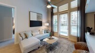 This single-floor residence is designed with a contemporary aesthetic and a functional open layout. The kitchen serves as a central highlight, featuring two-tone cabinetry — warm wood-grain lower cabinets paired with crisp white uppers — complemented by white quartz countertops, a subway tile backsplash, stainless steel appliances, and a large center island with seating. Elevated ceilings throughout the kitchen and adjoining spaces lend an airy, expansive feel.

The living area benefits from soaring ceilings and floor-to-ceiling windows with access to an outdoor area, allowing abundant natural light to fill the space. A ceiling fan adds a practical touch to this comfortable gathering space. A secondary sitting room, also with oversized windows, offers versatility as a guest room or lounge.

A dedicated flex room provides built-in shelving and direct sightlines to the kitchen, making it ideal as a home office or study. Light wood-tone flooring runs through the main living areas, transitioning to plush carpet in the bedrooms.

The primary bedroom is bright and serene, with large windows and a connected bathroom featuring a soaking tub, tiled shower surround, quartz vanity, and a walk-in closet. A second bathroom mirrors the refined finishes found throughout the residence.