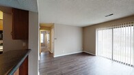 This single-floor unit is thoughtfully laid out to maximize functionality across its living spaces. The living room serves as a central gathering area, finished with dark hardwood-style flooring that extends throughout the main areas. Neutral beige walls and a textured ceiling provide a clean, understated backdrop, while a sliding glass door fitted with vertical blinds allows natural light to fill the space and provides access to the outdoors.

The kitchen is efficiently designed, featuring warm wooden cabinetry with ample upper and lower storage, dark countertops, and essential appliances including a refrigerator, electric range, microwave, and dishwasher. The hardwood-style flooring continues here, maintaining visual continuity with the main living area.

The bedrooms are carpeted for added comfort and warmth, each finished with the same neutral tones. At least one bedroom includes a walk-in closet and a window that introduces natural light. The bathroom is well-appointed with a wooden vanity, dark granite-style countertop, a single sink, and a full tub-shower combination with a clean white surround. Hardwood-style flooring in the bathroom ties cohesively to the rest of the unit's design.
