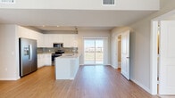 This well-designed two-story home offers 2 bedrooms, 3 bathrooms, and a thoughtful layout spread across two floors. The main floor, which comprises the larger portion of the home, features an open-concept kitchen and living area bathed in natural light from a sliding glass door that leads to a balcony with outdoor views. The kitchen is outfitted with white cabinetry, a subway tile backsplash, stainless steel appliances, and a central island with a white countertop, illuminated by pendant lighting overhead. Light hardwood flooring runs throughout the main level, lending a clean and contemporary feel. A dedicated entrance and a bathroom with a floating white vanity, brushed nickel fixtures, and a framed mirror round out the first floor. Upstairs, the carpeted second floor houses both bedrooms, including a generously sized primary bedroom with its own closet. The walk-in closet features wire shelving and a natural light-filled window with views of the surrounding landscape. The bathrooms are finished with modern hardware, including a full tub-shower combination lined with classic white subway tile. Soft neutral tones, plush carpeting in the bedrooms, and consistent modern detailing create a cohesive and comfortable living environment throughout.