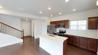 This two-story home is thoughtfully designed with a clean, modern aesthetic throughout. The kitchen serves as a central hub on the main floor, showcasing rich dark-wood cabinetry, light quartz countertops, and a full suite of stainless steel appliances including a French door refrigerator, electric range, and built-in microwave. A large central island with an undermount sink provides additional workspace and a natural gathering point. Dark hardwood-style flooring runs throughout the main level, complementing the recessed lighting overhead and neutral wall tones.

A half bath on the main floor features a pedestal sink, oval mirror, and a window that allows natural light in. Upstairs, the bedrooms are finished with plush carpeting and generous windows that bring in neighborhood views. The primary bedroom connects to a walk-in closet with dual hanging rods and shelving, alongside a private en-suite bathroom featuring a glass-enclosed walk-in shower and dark wood vanity. An additional full bathroom includes a tub-shower combo, dark countertop vanity, and a bright window. The home's overall palette of neutral tones and consistent finishes creates a cohesive, move-in-ready environment.