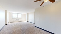 Located at 5325 S Cottage Grove Ave in Chicago's Washington Park neighborhood, this single-floor residential unit offers a clean, functional layout with a neutral color palette throughout. The spacious living area is carpeted and features a ceiling fan, a wall-mounted air conditioning unit, and large windows that flood the room with natural light while framing views of the surrounding cityscape and treetops. An adjacent open area extends the living space, benefiting from additional sunlight streaming in at angle across the carpet.

The kitchen is appointed with rich, dark cherry wood cabinetry that extends to the upper walls, complemented by granite-style countertops, hardwood-style flooring, and white appliances including a gas range and refrigerator. A flush-mount ceiling light keeps the kitchen well-lit.

The bedrooms are carpeted and bright, each featuring windows with outdoor views and built-in closets with hanging rods. One bedroom includes a convenient en-suite bathroom connection. The bathroom is finished with white tile surrounding the tub-shower combination, a wood-framed vanity with a single-basin sink, and a mirrored medicine cabinet above.

Baseboard heating is present throughout, and the overall layout is efficient and well-organized, making practical use of every area.
