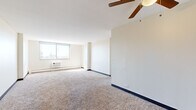 Located at 5325 S Cottage Grove Ave in Chicago's Washington Park neighborhood, this single-floor residential unit offers a clean, functional layout with a neutral color palette throughout. The spacious living area is carpeted and features a ceiling fan, a wall-mounted air conditioning unit, and large windows that flood the room with natural light while framing views of the surrounding cityscape and treetops. An adjacent open area extends the living space, benefiting from additional sunlight streaming in at angle across the carpet.

The kitchen is appointed with rich, dark cherry wood cabinetry that extends to the upper walls, complemented by granite-style countertops, hardwood-style flooring, and white appliances including a gas range and refrigerator. A flush-mount ceiling light keeps the kitchen well-lit.

The bedrooms are carpeted and bright, each featuring windows with outdoor views and built-in closets with hanging rods. One bedroom includes a convenient en-suite bathroom connection. The bathroom is finished with white tile surrounding the tub-shower combination, a wood-framed vanity with a single-basin sink, and a mirrored medicine cabinet above.

Baseboard heating is present throughout, and the overall layout is efficient and well-organized, making practical use of every area.