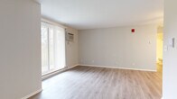 This 1-bedroom, 1-bathroom residence is thoughtfully arranged across a single floor, offering an efficient and comfortable living layout. The spacious living room is a standout feature, finished with light-toned luxury vinyl plank flooring that runs throughout the main living areas. Large floor-to-ceiling windows dressed with vertical blinds flood the room with natural light, while a wall-mounted air conditioning unit and baseboard heating ensure year-round comfort. Neutral gray walls create a clean, versatile backdrop throughout the space. The bedroom provides a generous retreat, featuring plush wall-to-wall carpeting, a ceiling fan with integrated lighting, a window with vertical blinds, and baseboard heating. Two closets offer ample storage to keep the space organized. The bathroom is finished with a full tub-and-shower combination with white tile surround and chrome fixtures. A dedicated laundry area houses a Rheem water heater and includes a built-in shelving rack, adding practical utility. The unit also features a front entry area, completing a well-rounded and functional floor plan suited for comfortable everyday living.