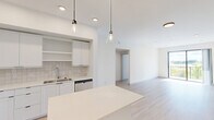 Located at 11200 Nicole Dr in Royal Palm Beach, FL, this single-story, 3-bedroom, 2-bathroom home offers a clean, modern aesthetic throughout. The open-concept kitchen and living area serves as the heart of the home, featuring a large white island, sleek white cabinetry with open shelving, a tile backsplash, stainless steel appliances, and stylish pendant lighting. Light wood-tone flooring runs continuously through the main living areas and bedrooms, creating a cohesive and airy feel. A connecting hallway leads to all three bedrooms, each finished with neutral walls and ample natural light. The primary bedroom includes direct access to a private balcony through a sliding glass door. Bedrooms are supported by five closets throughout the home, including a generously sized walk-in closet with wire shelving systems. The primary bathroom features large-format white tile flooring, a glass-enclosed walk-in shower, and a vanity with drawer storage. A dedicated laundry area adds everyday convenience. The overall design is bright and minimalist, with a consistent white-and-neutral palette that enhances the sense of openness across the entire floor plan.