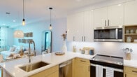 Located at 180 Boardwalk in Long Beach, NY, this one-bedroom, two-bathroom residence at The Breeze offers a thoughtfully designed coastal-modern living experience. Light wood flooring flows throughout, complementing the clean white walls and creating a bright, airy atmosphere across the open-concept layout.

The combined kitchen and living area serves as the heart of the home. The kitchen is outfitted with two-tone cabinetry — warm wood lower cabinets paired with white upper cabinets — along with a white quartz peninsula with bar seating, stainless steel appliances, a deep undermount sink, and pendant lighting. The living area features large black-framed windows that flood the space with natural light and offer outdoor views, while decorative wall art adds a coastal character to the room.

The spacious primary bedroom includes direct access to a private balcony through floor-to-ceiling glass doors, bringing in generous natural light and outdoor views. A dedicated closet and additional storage complete the bedroom.

Both bathrooms are finished with tile flooring, warm wood vanities, white countertops, and LED-lit mirrors, offering a clean, contemporary aesthetic. A hallway connects all rooms efficiently, maintaining a smooth and functional flow throughout the residence.