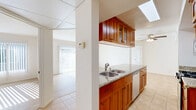 Located at 6645 Woodman Ave in the Van Nuys neighborhood of Los Angeles, this 2-bedroom, 2-bathroom residence offers a well-organized single-floor layout designed for comfortable everyday living. The open-concept kitchen and living area serves as the heart of the home, featuring warm-toned wood cabinetry with glass-front upper cabinets, granite countertops, a peninsula with a double stainless steel sink, and stainless steel appliances including a gas range and microwave. A skylight overhead brightens the kitchen, while a ceiling fan enhances airflow throughout the shared living space. Light tile flooring runs through the kitchen and bathrooms, while the living areas and bedrooms showcase light hardwood-style flooring that adds warmth throughout. The living room opens directly onto a private balcony through sliding glass doors with vertical blinds, filling the space with generous natural light. Both bedrooms are bright and airy, with large sliding glass or window access and mirrored closet doors. The two bathrooms are consistently appointed, each featuring granite-topped vanities with wood cabinetry and a tub-shower combination enclosed by sliding frosted glass doors. A hallway connects the main living areas to the bedrooms, with additional closet storage provided throughout the unit.