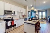 This well-appointed single-floor residence offers a thoughtfully designed open-concept layout that seamlessly connects the kitchen, dining, and living areas. The kitchen is a standout feature, showcasing crisp white shaker cabinetry, granite countertops, a subway tile backsplash, and a full suite of stainless steel Whirlpool appliances including a side-by-side refrigerator, range, microwave, and dishwasher. A central island with seating and pendant lighting serves as an elegant focal point, perfect for casual dining and entertaining. The living area is anchored by a bold teal accent wall adorned with a curated gallery of artwork, creating a vibrant and inviting atmosphere. Large glass doors lead to a private balcony, flooding the space with natural light and offering open outdoor views. The primary bedroom features a warm olive accent wall, a spacious walk-in closet, and a well-sized ensuite bathroom with granite countertops, white cabinetry, and subway tile shower surround. A second bedroom benefits from generous natural light through large windows with scenic views. The second bathroom mirrors the same refined finishes found throughout. Light wood-tone flooring ties the entire space together, contributing to a clean, modern aesthetic.