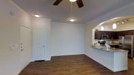 This single-floor residence offers a clean and functional layout designed for comfortable everyday living. The main living area is finished with rich, dark hardwood flooring that extends throughout, creating a warm and cohesive aesthetic. Crown molding along the ceiling adds a refined architectural detail, while a ceiling fan with integrated lighting provides both comfort and illumination. The space is bright and open, with neutral white walls that enhance the sense of airiness.

A rounded archway connects the living area to the kitchen, creating an open, flowing transition between spaces. The kitchen features dark espresso-toned cabinetry, stainless steel appliances including a microwave and range, and a granite countertop that extends to form a convenient breakfast bar. A pendant light fixture above the bar area adds a stylish finishing touch.

An interior door off the main living space provides access to additional areas of the home. The overall design balances practicality with subtle elegance, making it a well-appointed and inviting space. The combination of classic molding details, modern kitchen finishes, and durable flooring gives the interior a polished, move-in-ready feel suited for a variety of lifestyles.