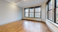 Located at 10 Grand River Ave in the heart of downtown Detroit, this one-bedroom, one-bathroom unit offers a well-appointed urban living experience across a generously sized single floor. The open layout is anchored by warm hardwood flooring that runs throughout, complementing the clean white walls and modern finishes found in every room.

A long hallway lined with large, black-framed windows welcomes you inside, flooding the space with natural light and offering views of the surrounding cityscape. The combined dining and living area features floor-to-ceiling-style windows on two walls, creating a bright, airy atmosphere with sweeping views of Detroit's downtown architecture.

The kitchen is a standout feature, outfitted with dark espresso cabinetry, granite countertops, stainless steel appliances, and a substantial granite-topped island with pendant lighting overhead—ideal for both cooking and casual dining.

The bedroom includes notably high ceilings, sliding panel closet doors, and access to additional closet space. Three closets total provide ample storage throughout the unit. The bathroom is finished with marble-style tile flooring, a granite vanity, dark cabinetry, and a built-in linen cabinet. A dedicated laundry area completes the layout.