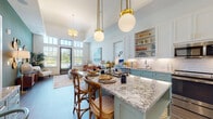 Located in the planned community of Celebration, FL, this single-floor residence combines modern design with thoughtful details throughout. The open-concept kitchen is a true centerpiece, featuring sage-green lower cabinetry paired with crisp white upper cabinets, a striking granite-topped island with seating, a classic subway tile backsplash, stainless steel appliances, and brass globe pendant lighting that adds a warm, contemporary touch. The kitchen flows seamlessly into the living area, which is anchored by soaring ceilings, a tray ceiling detail, and a wall of tall windows with transom panes that flood the space with natural light and offer views of the surrounding greenery. The primary bedroom continues the airy feel with elevated ceilings, dual windows, and ample natural light. Its en-suite bathroom is elegantly appointed with a double granite-topped vanity, brass hardware accents, and a spacious glass-enclosed walk-in shower. A second bedroom provides a comfortable and well-lit retreat, served by a full bathroom complete with a soaker tub, tiled surround, and coordinating granite vanity. Rich hardwood-style flooring runs throughout the main living areas, tying together a cohesive, upscale aesthetic that defines this well-appointed Celebration residence.