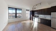 Located at 1315 W St NW in Washington, DC's lively U Street Corridor, this apartment offers a thoughtfully designed single-floor layout with contemporary finishes throughout. The open-concept living and kitchen area serves as the heart of the unit, where large, black-framed windows flood the space with natural light and frame views of the surrounding cityscape. Track lighting above the kitchen complements the abundant sunlight, ensuring the space is well-lit at all hours.

The kitchen is equipped with a full suite of stainless steel appliances, including a range, microwave, dishwasher, and refrigerator. Rich, dark espresso cabinetry provides ample storage and contrasts handsomely against the light countertops and white walls. Hardwood flooring extends throughout the main living areas, adding warmth and continuity to the open layout.

The bedroom features plush carpeting, clean white walls, and a large window with city views, creating a calm and comfortable retreat. A hallway with a louvered closet door connects the main living areas to the private spaces. The bathroom is finished with tile flooring, a dark-cabinet vanity with a white countertop, and a full tub-shower combination. The overall aesthetic is clean, modern, and move-in ready.