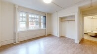 Located on the fifth floor at 929 SW Salmon St in the heart of Portland, Oregon, this studio apartment offers a thoughtfully arranged single-floor layout. The entrance opens into a bright, open living area finished with light hardwood-style flooring and white textured walls, creating a clean, neutral backdrop throughout. A large multi-pane window floods the main room with natural light while providing views of the surrounding cityscape, and a dedicated closet with a hanging rod offers practical storage. The galley-style kitchen is efficiently designed, featuring dark cabinetry with silver hardware, white countertops, a gas range, and a stainless steel refrigerator — all arranged along parallel walls for easy workflow. The full bathroom is finished in crisp white tones, with wainscoting detail, a standard toilet, and a soaking bathtub with overhead shower rigging. A second closet near the entrance adds additional storage. The textured popcorn ceilings and consistent light flooring tie the space together, giving the apartment a cohesive and functional feel suited to urban living in one of Portland's central neighborhoods.