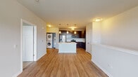 This single-floor residence in Romeoville, Illinois offers a well-designed open-concept layout that promotes a seamless flow between living and kitchen areas. The kitchen serves as a focal point of the space, showcasing rich dark cabinetry paired with light countertops and a white center island. Stainless steel appliances — including a refrigerator, electric range, over-the-range microwave, and dishwasher — provide a modern, functional cooking environment. Pendant lighting suspended above the island adds a refined touch. Wood-style hard surface flooring extends throughout the main living areas, contributing warmth and visual continuity.

A dedicated in-unit laundry area features a stacked washer and dryer, offering practical convenience. The living area is generously proportioned, with a built-in ledge along one wall providing an architectural detail and display opportunity. Natural light filters in through window-blind-equipped windows, offering views of the surrounding greenery.

The bedroom is carpeted for comfort and includes a window with outdoor views. The bathroom is clean and functional, featuring a dark-toned vanity, a tub-shower combination, and light wood-style flooring. Overall, the space presents a contemporary and cohesive aesthetic throughout.