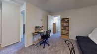 This single-floor residential unit offers a practical and functional layout across several well-defined living spaces. The living and dining area serves as the heart of the home, featuring plush carpeting and a ceiling fan with integrated lighting. The open sightline into the secondary bedroom creates a sense of added depth throughout the shared space.

The kitchen is efficiently designed with white cabinetry, light countertops, an under-cabinet sink, and ample storage provided by both upper and lower cabinets. The layout makes thoughtful use of available space, keeping essentials close at hand.

The primary bedroom is carpeted and includes a reach-in closet with bifold doors and built-in shelving. A window allows natural light to fill the room with views of surrounding greenery. The secondary bedroom also features carpet flooring, a window with blinds, and additional storage space, making it equally well-suited for use as a guest room or home office.

A dedicated office or flex room provides further versatility, complete with carpet, a door connecting to adjacent spaces, and room for a desk and bookshelf.

The bathroom retains a vintage character with its distinctive pink wall and floor tile, accented by a white vanity with a mirrored medicine cabinet and overhead lighting.

Overall, the unit provides a comfortable, well-organized living environment with consistent finishes throughout.