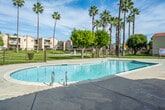Located at 1439 North Lilac Avenue in Rialto, California, this two-story residential community offers a well-appointed outdoor environment designed for comfort and leisure in the heart of the Inland Empire. The complex is built in a classic Spanish-influenced architectural style, characterized by stucco exteriors, red-tiled roof accents, and private balconies that overlook the communal grounds.

At the heart of the property lies a generously sized swimming pool with clear, blue water, complemented by an adjacent spa. The pool area features a spacious concrete deck ideal for lounging, along with a poolside utility structure and safety fencing throughout. Towering fan palms and mature shade trees are scattered across the well-maintained green lawns, lending the outdoor spaces a resort-like atmosphere beneath the wide Southern California sky.

The grounds are secured with iron fencing and include a gated entry point that leads to a dedicated parking area with covered carport spaces. The open layout of the common areas encourages an active outdoor lifestyle, with pathways connecting the various sections of the property. The combination of lush landscaping, ample outdoor amenities, and Mediterranean-inspired architecture makes this community a distinctive and inviting residential setting in Rialto.