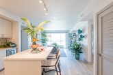 Located on the fifth floor at 130 Stockton in San Jose, California, this thoughtfully designed residence offers a bright and contemporary living experience. The open-concept layout connects the kitchen and living areas seamlessly, creating a welcoming flow throughout the space. The kitchen is outfitted with crisp white cabinetry, a mosaic tile backsplash, stainless steel appliances including a refrigerator, range, and built-in microwave, and a generously sized island with a quartz countertop and bar seating — ideal for both cooking and casual dining. Light hardwood-style flooring runs through the main living areas, enhancing the airy, modern aesthetic. The living room is anchored by a large picture window that frames views of the surrounding San Jose cityscape, filling the space with abundant natural light. The bedrooms are carpeted for comfort, each with windows providing additional natural light and views. Two well-appointed bathrooms feature modern floating vanities, clean white finishes, and light wood-tone flooring. Track lighting and recessed fixtures provide versatile illumination throughout. The unit's cohesive design, neutral palette, and quality finishes make it a refined and functional home in the heart of San Jose.