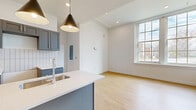 Located at 25 Public Square in Willoughby, OH, this thoughtfully designed one-bedroom, one-bathroom residence offers a clean, modern aesthetic across its single floor. Light hardwood flooring runs throughout, tying each room together with warmth and continuity.

The open-concept kitchen and living area serves as the heart of the unit. The kitchen is equipped with slate-blue shaker cabinetry, white quartz countertops, a subway tile backsplash, and a central island with an undermount stainless steel sink. Dramatic black pendant lights hang above the island, adding a contemporary touch. Large multi-pane windows flood the living area with natural light and offer views of the surrounding streetscape.

The bedroom is a comfortable, well-proportioned room featuring its own ceiling fan, a window with natural light, and direct access to a dedicated walk-in closet with built-in shelving and hanging rods — providing excellent storage.

The bathroom is a standout space, finished with classic white penny tile flooring, bold teal vertical wall tiles, a glass-enclosed walk-in shower, and a gray vanity with brushed gold hardware that echoes the kitchen's design language.

A utility room and additional closet round out the layout, ensuring practical storage and functional living. The unit's cohesive, modern finishes and bright interiors make it a refined and move-in-ready residence.