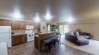 Located at 3755 Eighth Ave S in Saint Cloud, Minnesota, this single-floor unit offers a practical and comfortable layout designed for everyday living. The open-concept kitchen and living area serves as the heart of the space, where warm medium-toned wood cabinetry lines the kitchen walls, providing ample storage alongside generous counter space. White appliances, including an electric range with overhead microwave and a full-size refrigerator, complete the kitchen. A peninsula with seating extends into the dining area, creating a natural gathering point that flows seamlessly into the carpeted living room. The living room benefits from multiple windows that bring in natural light and offer views of the surrounding greenery, with sliding glass doors opening to a balcony. Tile flooring in an earthy stone-like pattern runs throughout the kitchen and bathroom areas. Two full bathrooms feature wood vanities with single-sink countertops, tiled floors, and shower-tub combinations. The bedrooms are carpeted and include windows with outdoor views. A dedicated laundry area houses a full-size washer and dryer with overhead shelving, adding convenience to the unit's overall functional design.