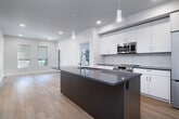 This thoughtfully designed two-bedroom, one-bathroom residence in Meridian, Idaho offers a clean, contemporary aesthetic with consistent light hardwood flooring flowing throughout the entire space. The open-concept kitchen and living area serves as the heart of the home, anchored by a substantial kitchen island with a quartz-style countertop, an undermount sink, and stylish pendant lighting. White cabinetry with a subway tile backsplash lines the walls, complemented by a full suite of stainless steel appliances including a refrigerator, range, and built-in microwave. Recessed lighting and natural light from multiple windows keep the living area bright and welcoming. Both bedrooms offer a calm, neutral palette with white walls, light wood floors, and windows that allow natural light and neighborhood views. Two closets provide practical storage throughout the unit. The bathroom features a white vanity with dark countertop, a backlit mirror, and a clean, functional layout with hardwood-style flooring. Dedicated closets add to the overall functionality of the space. The unit's modern finishes, consistent color palette, and efficient layout make it a well-appointed residence in a contemporary Meridian community.