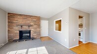 Located at 21215 Detroit Rd in Rocky River, OH, this one-bedroom, one-bathroom residence offers a thoughtfully laid-out single-floor plan with a comfortable and functional design. The living room serves as the centerpiece of the home, highlighted by a striking full-wall brick fireplace that adds warmth and character to the space. A trio of windows along one wall invites generous natural light, casting bright patterns across the plush gray carpeting. The room connects seamlessly to the entryway and a pass-through window opening to the kitchen, enhancing the open feel of the layout. The kitchen features white cabinetry, a stainless steel sink, light countertops, and wood-look flooring, along with a dishwasher and refrigerator. A hallway connects the living areas to the private bedroom, which is a generously sized retreat with carpet flooring, a ceiling fan, a closet, and a window with natural light. The bathroom is well-appointed with a white vanity, a tub-shower combination with tiled surround accented by warm-toned tile trim, and wood-look flooring. Throughout the home, neutral gray walls and clean white trim create a cohesive, move-in ready aesthetic.