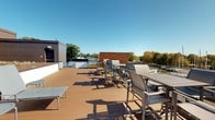 Located at 422 E Boston Post Road in Mamaroneck, NY, this rooftop deck offers an elevated outdoor retreat with sweeping open-air views of the surrounding neighborhood, mature tree canopy, and clear skies. The deck is finished with warm-toned composite wood planking that provides both durability and a refined aesthetic underfoot. A contemporary wood privacy screen adds a stylish architectural element while offering a degree of separation from adjacent structures. The space is thoughtfully furnished with high-top bar seating, dining chairs, and lounge benches, making it well-suited for both casual relaxation and social gatherings. Glass railings along the perimeter preserve unobstructed sightlines across the roofline and into the greenery beyond. In addition to the rooftop amenity, the space includes a well-designed custom closet system featuring adjustable shelving and cabinetry finished in a soft gray wood-grain laminate. Crisp, paneled cabinet doors complement the neutral palette, while modular shelving components offer flexible organization options. Together, the rooftop deck and interior storage space reflect a focus on functional design and quality finishes throughout.