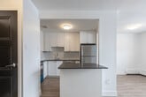 Located at 836 Talwood Dr in Peterborough, Ontario, this well-appointed 2-bedroom, 1-bathroom unit offers a thoughtfully designed layout across a single floor. The open-concept kitchen, dining, and living area serves as the heart of the home, featuring crisp white shaker-style cabinetry, a classic subway tile backsplash, dark countertops, and a full suite of stainless steel appliances including a refrigerator, dishwasher, stove, and over-the-range microwave. A central island provides additional prep and dining space, seamlessly connecting the kitchen to the living area. Light hardwood-style flooring runs throughout, complementing the bright, neutral palette of white walls and clean white trim. The primary bedroom is a comfortable size, filled with natural light from a large window overlooking the surrounding neighbourhood. The second bedroom is equally bright and versatile. Both rooms feature bold dark-panelled interior doors that add a striking contrast to the light interior. The bathroom is finished with white subway tile surrounding a full soaker tub and shower. A private balcony with large floor-to-ceiling windows offers pleasant outdoor views, completing this clean and modern living space.