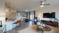 This single-floor residence offers a thoughtfully designed open-concept layout that seamlessly connects the living, dining, and kitchen areas. The living room is a bright and welcoming space, featuring wood-look flooring, a ceiling fan, and large windows dressed with teal drapes that invite abundant natural light and views of the surrounding area. A comfortable seating arrangement centers around a woven area rug and a round wood coffee table, creating an inviting atmosphere.

The kitchen is well-equipped with stainless steel appliances, light granite countertops, wood-toned cabinetry, a white subway tile backsplash, and a breakfast bar with leather-upholstered seating. Adjacent to the kitchen, the dining area is anchored by a striking shiplap accent wall in a weathered gray finish, adding warmth and texture to the space. A patio door provides additional natural light and outdoor access.

The bedroom is a serene retreat with dual windows overlooking the exterior, wood-look flooring, a ceiling fan, and ample space for furnishings. The bathroom features durable wood-look flooring, a soaking tub, and a built-in open shelving unit for organized storage. Throughout the residence, a cohesive neutral palette with modern finishes creates a clean, contemporary aesthetic.