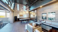 Located at 412 Madison St in Oakland, CA, this single-floor space showcases a compelling blend of industrial and contemporary design. The interior is defined by dramatically tall ceilings with exposed ductwork and dark ceiling panels, creating an expansive, loft-like atmosphere. Large-format gray tile flooring flows throughout, unifying the distinct functional zones.

A striking sculptural chandelier composed of clustered globe pendants serves as a focal point above the dining area, which features a substantial white-topped table with modern black chairs. Adjacent to this is a kitchenette outfitted with warm wood cabinetry, a white countertop, and a black refrigerator. A detailed cityscape mural runs along the white wall above, adding an artistic layer to the space.

A floor-to-ceiling glass partition separates a private meeting or breakout room, maintaining visual openness while providing acoustic separation. The lounge area is anchored by a reclaimed wood accent wall that adds warmth and texture, complemented by a sectional sofa, woven armchairs, leather ottomans, a large-screen TV, and curated artwork.

The space extends outdoors to a covered terrace featuring a metal pergola, a long communal dining table, and sweeping views of the Oakland skyline and surrounding hills.