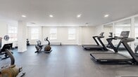 Located at 2101 Reamer Dr in Barrington, NJ, this dedicated exercise room offers a clean, functional fitness environment designed to support a variety of workout routines. The single-level space is generously sized, providing ample room to move freely between equipment without feeling cramped.

The room features a durable dark rubberized flooring ideal for high-traffic fitness use, complemented by crisp white walls and recessed lighting that keeps the space bright and energizing. A full-wall mirror along one side visually expands the room while allowing users to monitor their form during workouts.

Multiple large windows line the walls, inviting natural light and offering views of the surrounding outdoors, creating an open and airy atmosphere. Structural columns are thoughtfully integrated into the layout without impeding the usable floor space.

Cardio equipment includes several NordicTrack treadmills and stationary recumbent bikes, offering options for both moderate and high-intensity cardiovascular training. A dedicated free weights area features a multi-tier dumbbell rack with a range of weights, barbells with weight plates, and a weight bench, catering to strength training needs. Baseboard heating ensures year-round comfort. The room is well-organized, clean, and ready to accommodate a full fitness regimen.