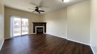 This single-floor residence offers a functional and comfortable layout with a cohesive design throughout. Rich, dark hardwood-style flooring runs through the main living areas, providing a warm contrast to the neutral, light-toned walls found throughout the space.

The open-concept living room is a standout area, anchored by a corner fireplace with a dark wood surround and tile detailing. A ceiling fan overhead and a sliding glass door inviting natural light complete the welcoming atmosphere of this central gathering space.

The galley-style kitchen is efficiently designed, featuring white cabinetry with ample storage above and below the counters, a double sink, light countertops, and white appliances including a refrigerator, electric range, and microwave. A peninsula counter extends into the living area, offering additional prep space and a natural division between the kitchen and living room.

The bedrooms offer plush carpeted flooring and generous closet space, including a mirrored sliding-door closet in one room and a louvered double-door closet accessible from another. Each bedroom benefits from natural light through windows.

The bathroom is well-sized, featuring a white vanity with under-sink storage, a framed mirror, dark hardware accents, and a full bathtub with shower — all set on the same dark hardwood-style flooring found throughout the home. Textured ceilings are present throughout, adding a classic residential character to the space.