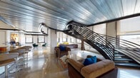 This two-floor loft showcases a compelling blend of industrial heritage and contemporary design. The main living area commands attention with its soaring ceilings clad in corrugated metal panels, exposed ductwork, and a dramatic curved black steel staircase with angular railings that serves as a sculptural centerpiece. Polished terrazzo floors reflect light throughout the open-plan space, which flows seamlessly between a generous living area and a sleek, modern kitchen. The kitchen features white cabinetry, subway tile backsplash, gray countertops, and stainless steel appliances.

The living space is framed by multiple large windows offering urban views, while whitewashed exposed brick walls add raw texture throughout. A mezzanine level, accessed via the statement staircase, overlooks the main floor and incorporates glass block partitions that allow light to filter between levels.

The bedrooms continue the industrial-chic aesthetic with whitewashed brick, soaring ceilings, glass block walls, and generous natural light. Bathrooms are well-appointed with glass-enclosed showers, modern vanities, and wood-look flooring. Additional utility space features an exposed concrete ceiling with built-in cabinetry, completing this architecturally distinctive loft.