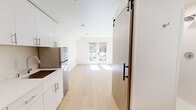 Located at 4612 Stone Way N in Seattle's vibrant Wallingford neighborhood, this thoughtfully designed studio unit makes efficient use of its compact footprint across a single floor. The open-concept layout seamlessly connects the kitchen and living areas, creating a bright and functional living space bathed in natural light.

The kitchen is outfitted with modern white cabinetry extending floor to ceiling, stainless steel appliances including a full-size refrigerator, an electric cooktop, wall oven, and built-in microwave — all set against clean white countertops. Light hardwood-style flooring runs throughout the unit, lending warmth and visual continuity to the space.

A sliding barn-style door with a matte black hardware accent adds a contemporary architectural detail, providing privacy to the bathroom. The bathroom is clean and minimalist, featuring a white vanity, toilet, and warm wood-toned flooring.

The living area is airy and open, anchored by a set of French doors that flood the space with natural light and offer views of a charming rock garden and lush greenery outside — a serene and distinctive outdoor backdrop. A bold red entry door adds a pop of color at the entrance. The unit also includes an electrical panel conveniently recessed into the wall. Overall, the space presents a clean, modern aesthetic ideal for efficient urban living.