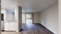 This single-floor unit offers a clean, modern layout with a practical and cohesive design throughout. The open-concept living area is finished with rich, dark hardwood-style flooring and neutral gray walls, creating a warm yet contemporary atmosphere. A large sliding glass door floods the living space with natural light and provides direct views of lush outdoor greenery, extending the sense of space beyond the interior. A baseboard heating system runs along the perimeter of the living area, ensuring year-round comfort.

The kitchen is thoughtfully separated from the living room by a partial wall, maintaining an open feel while defining each area. It features white cabinetry, a stainless steel sink, stainless steel appliances including a refrigerator, electric range, and dishwasher, all set atop light hardwood-style flooring with a bright overhead light panel.

The bedroom is a peaceful retreat, carpeted in soft neutral tones and naturally lit by a window with horizontal blinds. A baseboard heater is present here as well, and the room offers ample space for furnishing.

The bathroom is straightforward and functional, complete with a full-size soaking tub with a shower, a toilet, and easy-to-maintain hardwood-style flooring. A textured ceiling is a consistent architectural detail found throughout the unit.