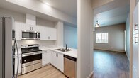 This thoughtfully designed single-floor residence offers a practical and modern layout across one bedroom, one bathroom, a living room, kitchen, and closet. The kitchen is a standout feature, outfitted with crisp white shaker cabinetry, light quartz countertops, and a full suite of stainless steel appliances including a French door refrigerator with ice dispenser, an electric range with overhead microwave, and a dishwasher. Light wood-style flooring runs throughout the kitchen, creating a clean, contemporary aesthetic complemented by soft blue accent walls.

The living room is open and airy, featuring the same light hardwood-style flooring, neutral grey walls, and a ceiling fan with a light fixture that adds both function and a finishing touch. A window invites natural light and views to the exterior, enhancing the sense of space.

The bedroom offers a cozy atmosphere with plush carpeting, soft neutral walls, and a window fitted with blinds for light control and privacy. The bathroom is cleanly finished with a white vanity, mirror, and light wood-style flooring that ties in with the rest of the unit. The overall design is modern and neutral, making this an inviting and functional living space.