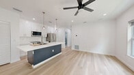 Located at 527 N Garden Ave in Clearwater, FL, this thoughtfully designed 3-bedroom, 2-bathroom unit offers a clean, modern aesthetic throughout. The open-concept kitchen and living area serves as the heart of the home, featuring white shaker cabinets, stainless steel appliances, a bold navy kitchen island with quartz countertops, globe pendant lighting, and a ceiling fan — all set atop light-toned wide-plank hardwood flooring that flows seamlessly through the entire space.

Each bedroom is bright and airy, equipped with ceiling fans and generous closet space, including louvered bi-fold closet doors in the primary bedroom. Two of the bedrooms provide direct access to private balconies with outdoor views of surrounding greenery, offering a refreshing indoor-outdoor connection.

Both bathrooms are finished with floor-to-ceiling marble-look tile, dark navy vanities, and brushed gold or chrome hardware. One bathroom features a frameless glass walk-in shower, while the other showcases a sleek, open wet-room layout. Additional conveniences include a dedicated laundry area, hallway, and two closets. The unit's crisp white walls, recessed lighting, and consistent modern finishes create a bright, polished atmosphere throughout.