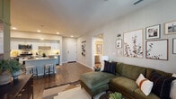 This single-floor residence offers a thoughtfully designed open-concept layout that seamlessly connects the living, dining, and kitchen areas. Rich hardwood-style flooring flows throughout the main living spaces, anchoring the warm yet modern aesthetic.

The kitchen is a functional centerpiece, featuring two-tone gray and white cabinetry, a tile backsplash, stainless steel appliances, and a peninsula island with seating for two — ideal for casual dining or entertaining. Pendant lighting adds a polished finishing touch overhead.

The living area is generously proportioned, with recessed lighting and a large window allowing natural light to fill the space. A dedicated entry foyer provides a clean transition into the home.

Two bedrooms offer distinct character: one features a shiplap accent wall and bright window with sheer curtains, while the other showcases an earthy, moody palette with wall-mounted planters and natural light filtered through blinds.

Two full bathrooms are finished with gray cabinetry, white quartz countertops, and wood-style flooring. The primary bath includes a double-sink vanity with a large mirror, while the secondary bath features a tub-shower combination with a clean white tile surround. Together, these spaces reflect a cohesive, contemporary design sensibility throughout.