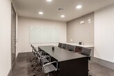 This single-floor commercial space in Overland Park, Kansas offers a thoughtfully designed professional environment with a clean, contemporary aesthetic throughout. The layout includes a well-appointed conference room anchored by a large dark rectangular table surrounded by ergonomic rolling chairs. A full-width glass whiteboard spans one wall, while textured tile accent panels add visual depth, and recessed lighting provides consistent, even illumination across the carpeted floor.

Private offices are outfitted with L-shaped dark wood desks paired with sleek blue task chairs and vibrant orange accent chairs, creating a balanced blend of functionality and style. Large windows in each office invite natural light and offer open views of the surrounding Overland Park landscape, enhancing the sense of space. Original artwork — including bold abstract and geometric pieces — is displayed prominently on the walls, contributing a curated, professional character to each room.

A dedicated lounge area provides a comfortable setting for informal meetings or relaxation, furnished with upholstered seating in neutral tones alongside wood-framed accent chairs. Striking red abstract canvas panels adorn the lounge walls, reinforcing the space's cohesive artistic identity. Recessed lighting and patterned carpet tie the overall design together throughout.