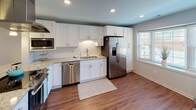 Located in Charlotte's 28211 zip code, this two-story home offers a thoughtfully designed layout with consistent, modern finishes throughout. Rich hardwood-style flooring flows across the main level, complementing the neutral gray and white color palette that creates a clean, cohesive aesthetic.

The main level centers around an updated kitchen equipped with white shaker cabinetry, granite countertops, stainless steel appliances including a refrigerator, dishwasher, and built-in microwave, and a stainless steel island vent hood. A peninsula with seating provides casual dining space, while pendant lighting and recessed fixtures illuminate the area. Adjacent to the kitchen, a charming bay window nook and a glass-paneled door bring natural light into the living areas. A spacious living room features shuttered windows and direct access to the outdoors.

The upper level features generously sized bedrooms carpeted in neutral tones. One bedroom includes dual windows alongside a distinctive circular porthole window, enhancing natural light and visual interest. A primary bedroom connects to an en-suite bathroom finished with a granite vanity and glass-enclosed walk-in shower. A second full bathroom on this level offers a granite vanity alongside a tub-shower combination, completing the home's well-rounded layout.