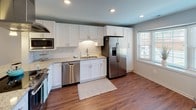 Located in Charlotte's 28211 zip code, this two-story home offers a thoughtfully designed layout with consistent, modern finishes throughout. Rich hardwood-style flooring flows across the main level, complementing the neutral gray and white color palette that creates a clean, cohesive aesthetic.

The main level centers around an updated kitchen equipped with white shaker cabinetry, granite countertops, stainless steel appliances including a refrigerator, dishwasher, and built-in microwave, and a stainless steel island vent hood. A peninsula with seating provides casual dining space, while pendant lighting and recessed fixtures illuminate the area. Adjacent to the kitchen, a charming bay window nook and a glass-paneled door bring natural light into the living areas. A spacious living room features shuttered windows and direct access to the outdoors.

The upper level features generously sized bedrooms carpeted in neutral tones. One bedroom includes dual windows alongside a distinctive circular porthole window, enhancing natural light and visual interest. A primary bedroom connects to an en-suite bathroom finished with a granite vanity and glass-enclosed walk-in shower. A second full bathroom on this level offers a granite vanity alongside a tub-shower combination, completing the home's well-rounded layout.