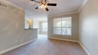 This single-story unit is designed with a cohesive, neutral color palette and thoughtful finishes throughout. The main living area features plush carpeting, crown molding, and a ceiling fan with a light kit. Multiple windows fitted with horizontal blinds allow natural light to filter through, while a set of French doors with a transom window provides direct access to an outdoor area, enhancing the sense of openness. A pass-through bar counter connects the living space to the kitchen, which is equipped with dark espresso cabinetry, granite-style countertops, hardwood flooring, and stainless steel appliances including a range and built-in microwave.

The bedroom is generously proportioned, featuring carpeted floors, crown molding, a ceiling fan, and a window overlooking greenery. Mirrored sliding closet doors open to a walk-in closet outfitted with built-in shelving for organized storage. The bathroom includes a dark-cabinetry vanity with a large mirror, tile flooring, and a tub-shower combination. A secondary bathroom offers a soaking tub and tiled surround. Overall, the unit presents a well-appointed, functional layout with consistent finishes and ample natural light throughout.