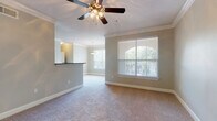 This single-story unit is designed with a cohesive, neutral color palette and thoughtful finishes throughout. The main living area features plush carpeting, crown molding, and a ceiling fan with a light kit. Multiple windows fitted with horizontal blinds allow natural light to filter through, while a set of French doors with a transom window provides direct access to an outdoor area, enhancing the sense of openness. A pass-through bar counter connects the living space to the kitchen, which is equipped with dark espresso cabinetry, granite-style countertops, hardwood flooring, and stainless steel appliances including a range and built-in microwave.

The bedroom is generously proportioned, featuring carpeted floors, crown molding, a ceiling fan, and a window overlooking greenery. Mirrored sliding closet doors open to a walk-in closet outfitted with built-in shelving for organized storage. The bathroom includes a dark-cabinetry vanity with a large mirror, tile flooring, and a tub-shower combination. A secondary bathroom offers a soaking tub and tiled surround. Overall, the unit presents a well-appointed, functional layout with consistent finishes and ample natural light throughout.