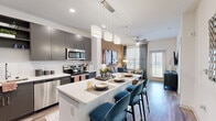 This single-floor, one-bedroom residence offers a smartly designed layout that maximizes every square foot with modern finishes and a cohesive aesthetic throughout. The open-concept kitchen is a standout feature, equipped with stainless steel appliances, dark charcoal cabinetry, light quartz countertops, and a generous island with seating for multiple guests — all illuminated by stylish pendant lighting overhead. Wood-style flooring runs throughout the main living areas, adding warmth and continuity to the space. The living room is anchored by a warm-toned accent wall and features a private balcony access door framed by large windows dressed with blinds and floor-length drapes, allowing for ample natural light. A ceiling fan overhead enhances comfort in this relaxed yet refined gathering space. The bedroom offers a serene retreat with soft carpet, large windows that invite natural light, a ceiling fan, and a dedicated closet for storage. The warm neutral wall tones and clean architectural lines found throughout the residence create a cohesive, contemporary ambiance that is both functional and inviting.