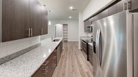 This single-story residence in Austin, Texas offers a thoughtfully designed open-concept layout with contemporary finishes throughout. The kitchen is a standout feature, showcasing dark espresso cabinetry, granite countertops, a subway tile backsplash, stainless steel appliances, and elegant pendant lighting. A built-in arched shelving nook adds a charming architectural detail that bridges the kitchen and living areas. The spacious living room is bathed in natural light and features wood-look vinyl flooring and a ceiling fan, with sliding glass doors opening to an outdoor patio area. Bedrooms are carpeted for comfort, each offering natural light through large windows with outdoor views. The primary bathroom is well-equipped with a double-sink vanity topped with granite, dark wood cabinetry, a large framed mirror, and wood-look flooring. A secondary bathroom includes a tiled shower-tub combination and matching finishes. A dedicated laundry room houses a full-size washer and dryer alongside the water heater. A smart thermostat is also present, adding a modern convenience. Consistent wood-look vinyl flooring, neutral walls, and cohesive dark cabinetry tie the entire space together with a clean, modern aesthetic.