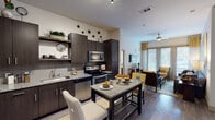 This well-appointed single-floor residence combines contemporary design with functional living across a thoughtfully arranged floor plan. The open-concept kitchen is outfitted with dark espresso cabinetry, granite countertops, a subway tile backsplash, and a full suite of stainless steel appliances, including a range, microwave, dishwasher, and refrigerator. A granite-topped kitchen island with bar seating provides additional dining and prep space, seamlessly connecting the kitchen to the main living area. Wide-plank wood-style flooring runs throughout the main living spaces, adding warmth and continuity. The living room is bright and welcoming, featuring large floor-to-ceiling windows and sliding glass doors that invite abundant natural light, complemented by a ceiling fan overhead. The bedrooms are comfortable retreats, each well-lit by generous windows and finished with plush carpeting. Both bathrooms echo the kitchen's design aesthetic with granite-topped dark vanities and wood-style flooring. Each bathroom provides access to a dedicated walk-in closet with built-in shelving and hanging rods, offering ample storage. The primary bathroom features notably high ceilings and a glass-enclosed walk-in shower, while the secondary bathroom is equally well-appointed with a vanity and adjacent walk-in closet with open shelving.