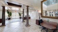 Located at 12025 Paul Eells Dr in North Little Rock, AR, this expansive single-floor facility offers a diverse array of amenity-rich spaces across a generous footprint. The entrance makes an immediate impression with towering fluted columns, large-format tile flooring, and glass double doors that flood the space with natural light. The office area features soaring ceilings, tile flooring, and a functional workspace layout with room for meetings. The living room is elegantly appointed with a dark brick fireplace, built-in shelving, an arched window, recessed lighting, and a ceiling fan, creating a warm and sophisticated atmosphere. The kitchen includes dark wood cabinetry, slate-toned countertops, stainless steel appliances, and tile flooring. The game room is a standout feature, offering hardwood-style flooring, a full-size pool table, ping pong table, wall-mounted TV, and bold gray accent walls with colorful artwork. Additional living areas provide comfortable lounge seating with modern décor. The indoor pool area is enclosed by exposed brick walls, arched openings, ceiling fans, and tile surround, offering a resort-like retreat. Two bedrooms and two hallways round out this well-appointed, multifunctional space.