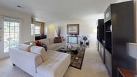 The Camden Premium in Ann Arbor, Michigan, presents a thoughtfully designed two-bedroom, two-bathroom floor plan across a single level. The expansive living room serves as the heart of the home, featuring plush carpeting, large windows that invite natural light, and generous space for both lounging and entertaining. The kitchen is outfitted with white cabinetry, dark granite countertops, stainless steel appliances including an electric range and refrigerator, and tile flooring that extends throughout the space. Both bedrooms are well-sized and carpeted, offering a calm retreat. The primary bedroom includes a walk-in closet with built-in shelving and an en-suite bathroom featuring a wide vanity with dark granite countertops, white cabinetry, and a tiled shower. The second bedroom benefits from a large window with outdoor views of greenery, providing a bright and airy atmosphere. The second full bathroom mirrors the refined finishes of the primary, with a similar vanity setup and a shower-tub combination. Additional storage is available throughout, including a dedicated utility closet. The overall design palette of neutral tones, dark accents, and consistent finishes creates a cohesive and polished living environment.