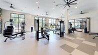 Located at 4805 Creek Cir in Cumming, GA, this expansive fitness center offers a comprehensive, single-floor layout designed to support a wide range of workout styles and fitness goals. The space is organized into distinct functional zones, providing an intuitive flow from one area to the next.

The main strength and cardio area features a generous selection of Precor selectorized machines, free weights, a full dumbbell rack, and multiple treadmills positioned along large floor-to-ceiling windows that frame lush outdoor views. Checkered rubber flooring provides both durability and a dynamic visual element throughout this zone.

A separate flex studio, enclosed by sleek black-framed glass partition walls, offers a dedicated space for functional training. This area features light wood-look flooring, a power rack, kettlebell storage, stability balls, and open floor space ideal for stretching or group classes. Motivational mural graphics and wall-mounted mirrors add energy and depth to the environment.

Throughout the facility, white walls and recessed lighting create a clean, bright atmosphere, while multiple large ceiling fans maintain comfortable airflow. Abundant natural light pours in from oversized windows on multiple walls, connecting the interior to the surrounding landscape. The overall design balances modern aesthetics with practical, high-performance functionality.